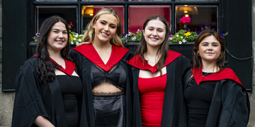 Four students wearing their graduation gowns outside the Usher Hall in Edinburgh