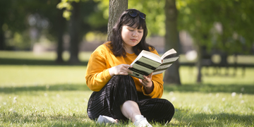 Student sitting under a tree at the park with a book