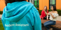 Resident Assistant facing away from the camera, showing their blue hoodie with 'Resident Assistant' on the back