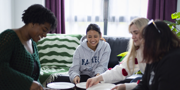 Four students sitting in the living area in student accommodation, handing out plates for a meal