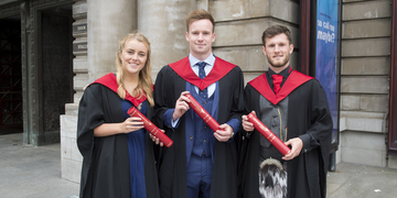 Three graduates outside Usher Hall holding Edinburgh Napier scrolls