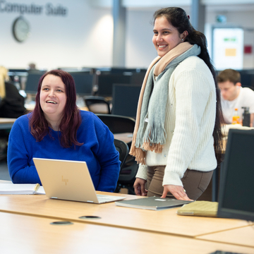 Two students standing in front of a laptop, smiling at someone else