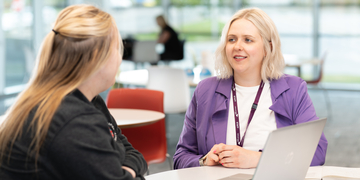 Member of staff talking to a student at a study table