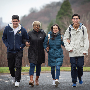 Four students in outdoor clothing and jackets walking together in a line with their arms linked
