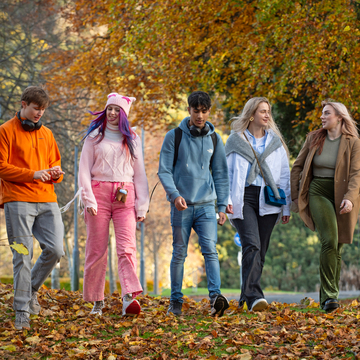 Five students in bright outdoor clothing, walking together through autumn leaves