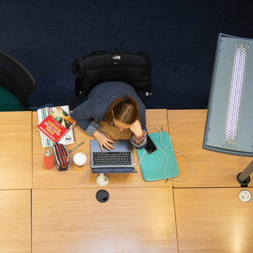 Overhead view of student studying in library, with laptop and notebooks