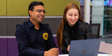 Two students in the library looking at a laptop screen together and smiling
