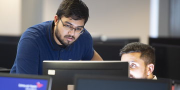 Student looking over computer screen on campus with someone sitting next to them