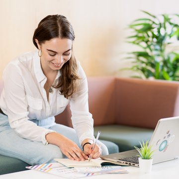 Student writing on notepad in front of laptop