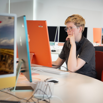 Student sitting in a bright room, looking at an orange computer screen
