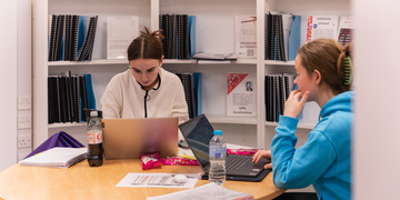 Two students sitting in library, working on their laptops