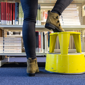 Image of feet standing on footstool to reach library shelf.