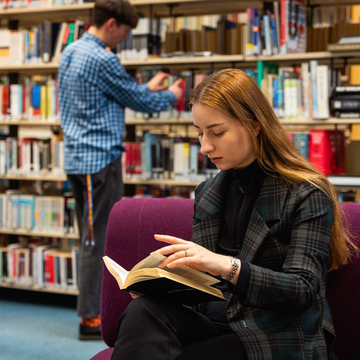 Student reading a book in front of Library bookshelves