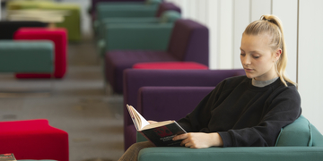 Student reading a book in a comfy chair in Sighthill LIbrary