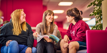 Three students sitting with a book on a sofa in the library