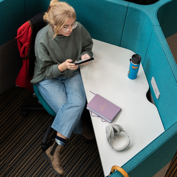 Student sitting in study booth with personal items, including headphones, a notebook and a drinks bottle