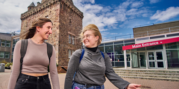 Two students walking across the courtyard at Merchiston campus, in front of the main entrance