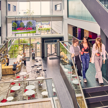 Three students walking down the stairs above the atrium at Sighthill campus