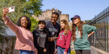 A group of students standing together, taking a selfie in front of Edinburgh Castle