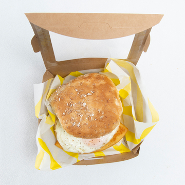 Top-down view of breakfast roll with fried egg in a brown takeaway box