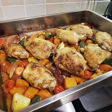 Roasted chicken thighs on bed of vegetables in baking tray