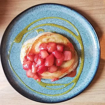 Pancakes on plate drizzled with syrup, with chopped strawberries on top