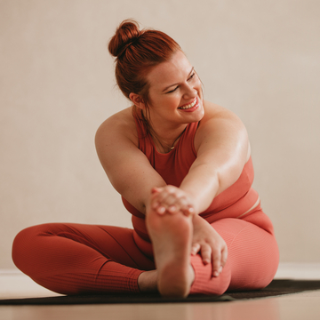 Woman with hair tied back wearing pink gym clothes stretching her leg with one hand in a yoga pose