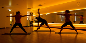 Silhouettes of students doing yoga in orange-lit studio