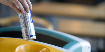 Person putting drinks can in recycling bin