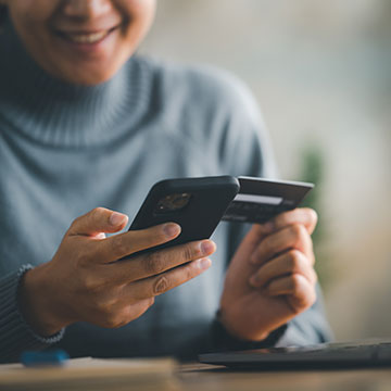Student looking down at their mobile phone in one hand and a debit card in the other
