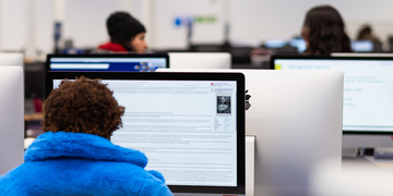 Student in blue fluffy hoodie working at a computer in the computing suite