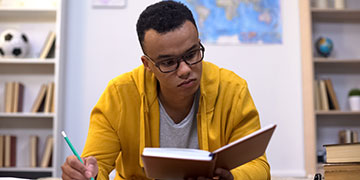 Student sitting looking over a book with a pencil in one hand