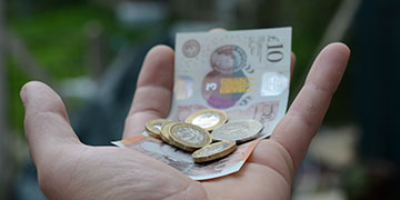 A hand holding a selection of bank notes and coins