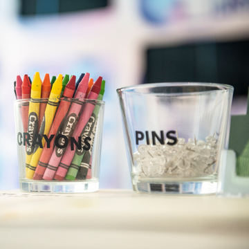 A glass jar of colourful crayons next to a glass jar of pins
