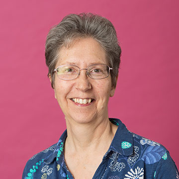 Staff headshot of Jenny Hall with short grey hair and glasses, wearing a patterned blue blouse