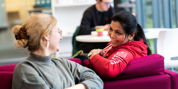 Two students leaning across a sofa to talk to each other