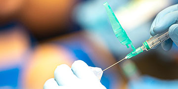 Close up of a gloved hand filling a needle for a vaccination
