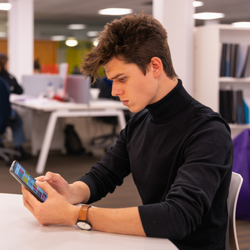 Student sitting at a desk using the Edinburgh Napier app on their mobile phone