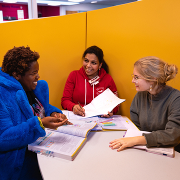 A group of students sitting in a study space, working together with laptops and notes