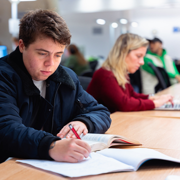 A student sitting in a study space, working on notes with a notepad and pencil