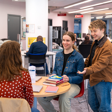A group of students sitting in a study area, talking to each other with their notebooks and laptops