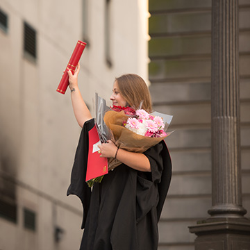 Student celebrating graduation with scroll and flowers