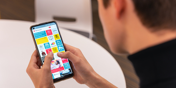 Student sitting at a desk, looking at the Edinburgh Napier app on a mobile phone