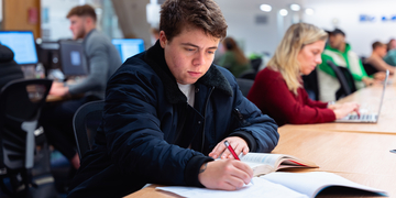 A student studying with an open book and pencil taking notes