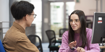 Two students discussing their studies by a computer