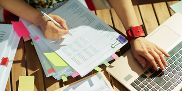 Various papers and notepads next to a laptop for study