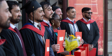 Graduating students wearing their graduation gowns outside the Usher Hall in Edinburgh, holding their certificates and flowers