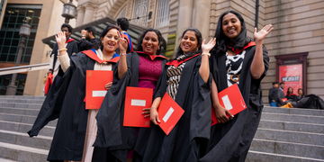 Graduating students wearing their graduation gowns outside the Usher Hall in Edinburgh, holding their certificates