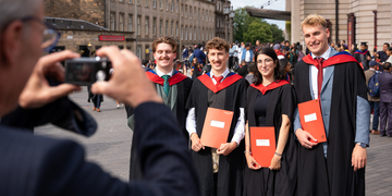 Graduating students wearing their graduation gowns outside the Usher Hall in Edinburgh, holding their certificates while posing for a photo
