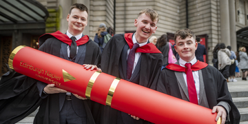 Graduating students wearing their graduation gowns outside the Usher Hall in Edinburgh, holding a giant scroll